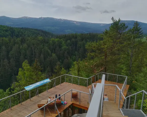 Drewniany punkt widokowy w Karpaczu z widokiem na góry i las. Dwie osoby odpoczywają na tarasie.