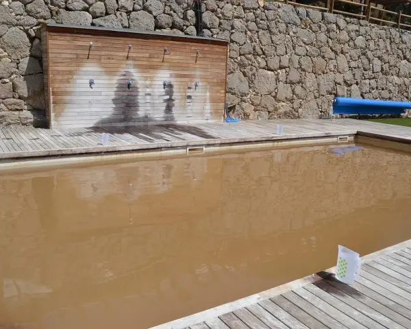 Piscina de sal con agua turbia y rodeada de madera. Al fondo, una pared de piedra y duchas.
