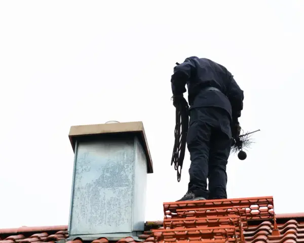 Kominiarz na dachu z narzędziami. Sprawdź, jaka jest opinia kominiarska cena za jego usługi.