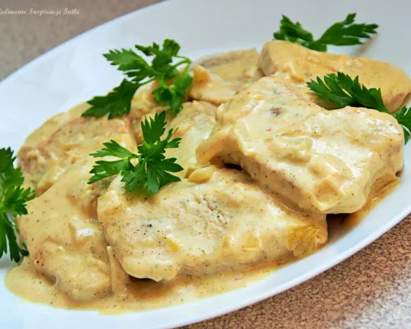 Filet z indyka w sosie śmietanowym, udekorowany natką pietruszki, prezentuje się apetycznie na białym talerzu.