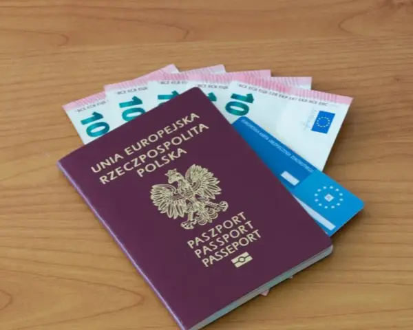 Polski paszport, euro i karta ubezpieczenia zdrowotnego na drewnianym tle.