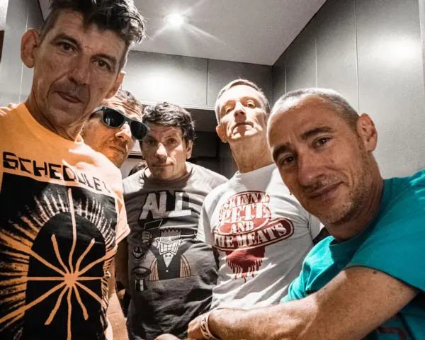 Cinq hommes aux têtes brûlantes, certains souriants, d'autres plus intenses, posent pour un selfie. Leurs t-shirts affichent des graphismes variés.