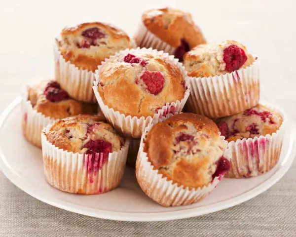 Stos muffinek z malinami na białym talerzu.