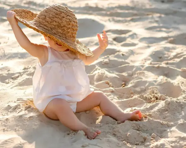 Liten bebis med stråhatt på stranden, njuter av solens värme.