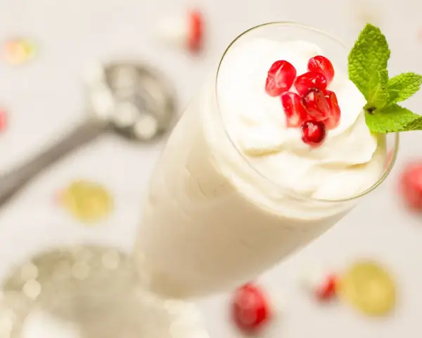 Creme double in einem Glas, garniert mit Granatapfelkernen und Minze. Ein Löffel liegt daneben.