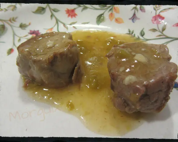 Dos trozos de solomillo al whisky en una salsa dorada, servidos en un plato con flores.