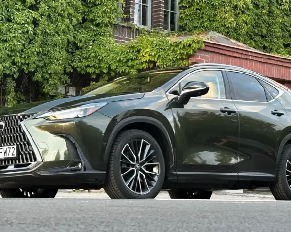 Ciemnozielony Lexus NX 450h+ plug-in zaparkowany przed budynkiem porośniętym bluszczem.