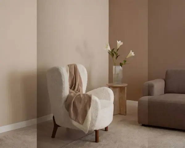 Gemütliches Wohnzimmer mit beigen und braunen Wandfarben. Ein flauschiger Sessel mit Decke und ein Sofa laden zum Entspannen ein.