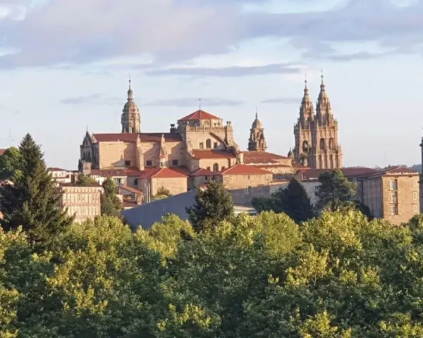 Majestatyczna katedra w Santiago de Compostela, cel pielgrzymek, wyłania się zza zieleni drzew.