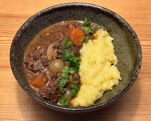 En mustig boeuf bourguignon med möra köttbitar, champinjoner, lök och morötter, serverad med krämigt potatismos.