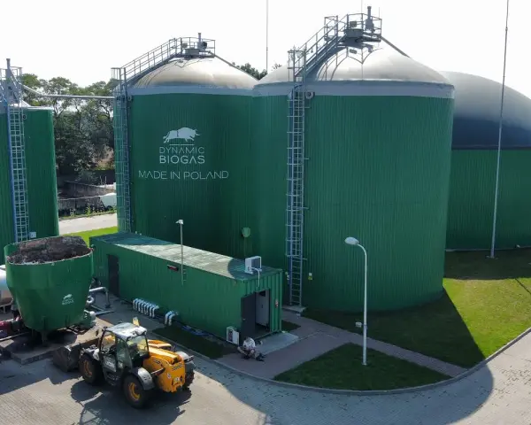 Zielone zbiorniki instalacji biogazowej, z logo "DYNAMIC BIOGAS MADE IN POLAND". Obok ładowarka i kontener.