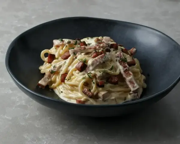 Pyszne spaghetti carbonara, jeden z klasycznych makaronów, podane w ciemnej misce, posypane natką pietruszki i kawałkami boczku.