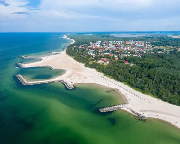 Malownicze plaże w Polsce z kamiennymi falochronami, zielonymi wodami Bałtyku i nadmorskim miasteczkiem w tle.