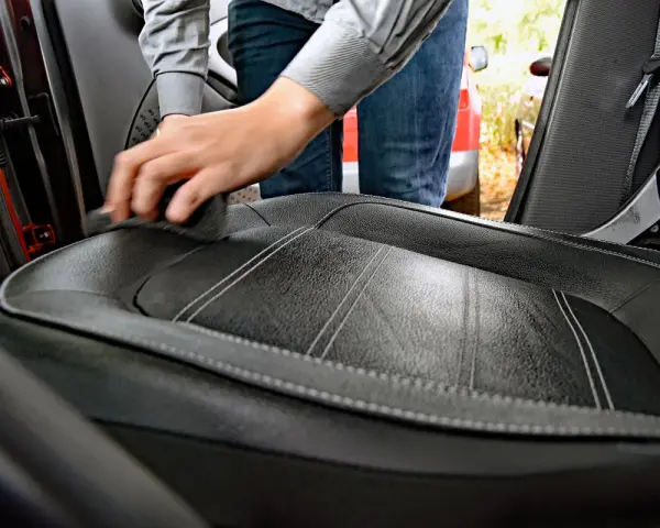 Hand reinigt Autositz aus Leder mit einem Tuch. Hausmittel für Leder reinigen sind eine gute Wahl.