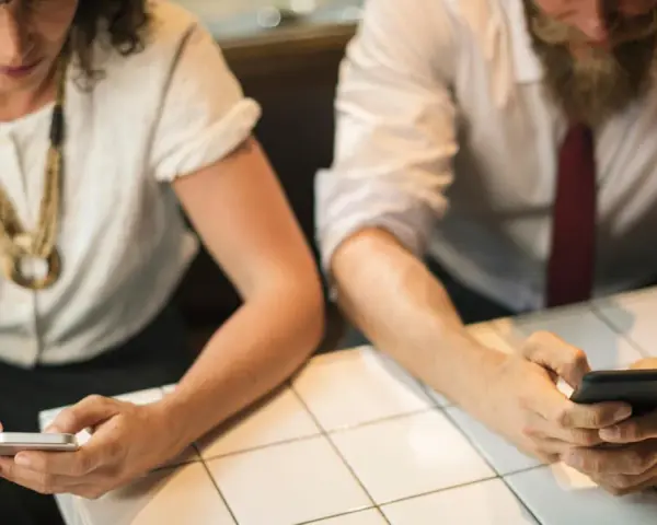 Zwei Personen sitzen an einem Tisch und schauen auf ihre Smartphones.