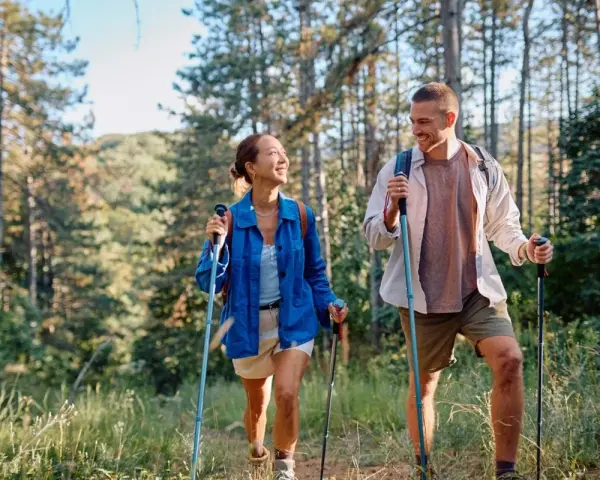 Coppia sorridente fa nordic walking tra gli alberi, godendosi i benefici di questa attività all'aria aperta.