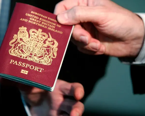 Dłoń podaje paszport biometryczny Wielkiej Brytanii. Widoczny herb i napis "PASSPORT".