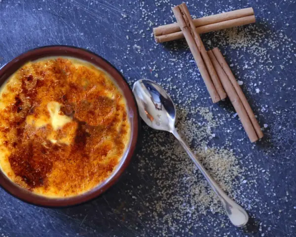 Cremige Crema Catalana mit karamellisierter Zuckerkruste, daneben Zimtstangen und Zucker.