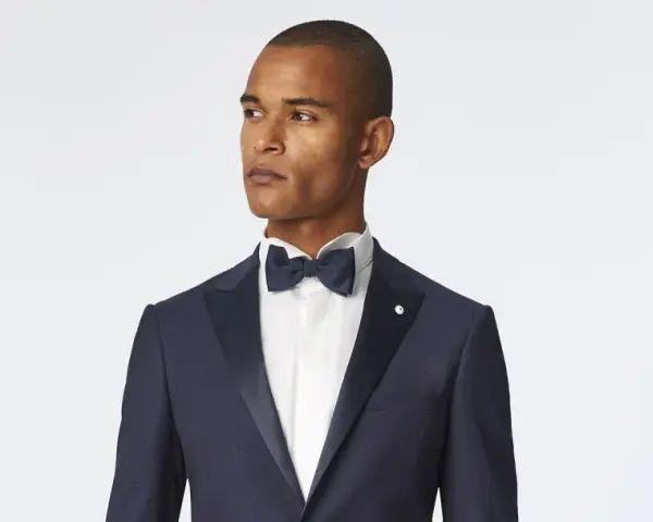 Uomo con smoking blu scuro, camicia bianca e papillon blu. Un look elegante per ogni occasione speciale.