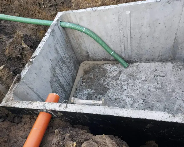 Montaż szamba betonowego 10m3. Widoczny betonowy zbiornik w wykopie, z podłączonymi rurami.