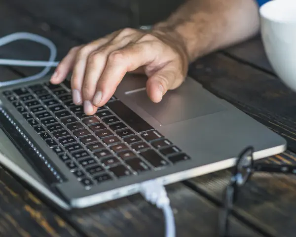 Dłoń na klawiaturze laptopa, przygotowująca się do twardego resetu. Obok biały kubek.