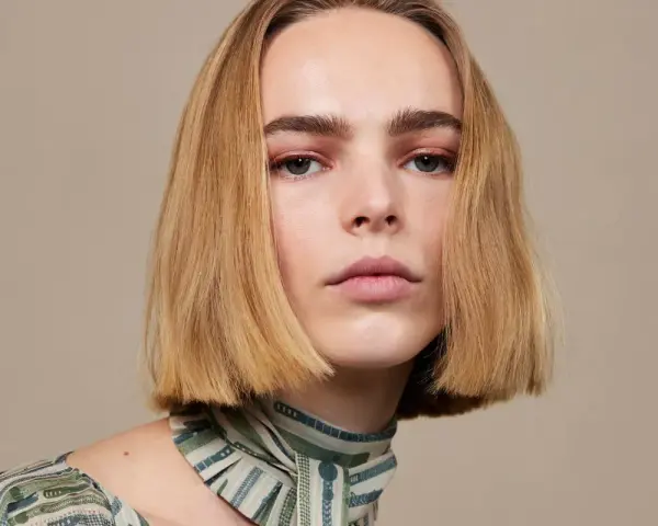 Modelka z subtelnym makijażem i fryzurą bob krótki tył, prezentuje się elegancko w bluzce z wzorem.