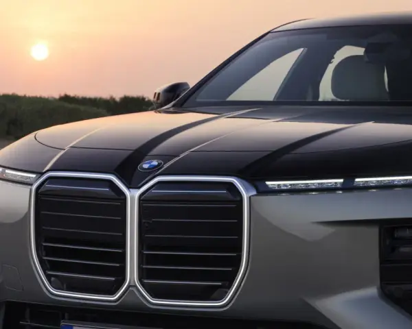 Przód luksusowego BMW M7 z podświetlaną atrapą chłodnicy i nowoczesnymi światłami, na tle zachodzącego słońca.