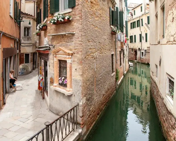 Un vicolo stretto e un canale a Venezia, con una donna e un cane seduti, tra i tanti **Venezia posti da visitare**.