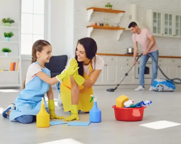 Mama i córka świętują wykonane obowiązki 9 latka w domu. Tata odkurza w tle.