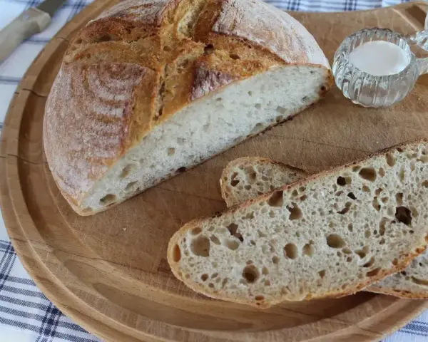 Chleb nocny na zakwasie, pokrojony na desce, z widocznym puszystym wnętrzem i chrupiącą skórką. Obok mała miseczka z solą.