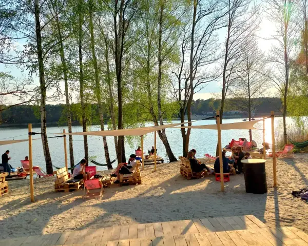 Relaks na piaszczystej plaży nad jeziorem. Ludzie odpoczywają w cieniu namiotów, tworząc przytulne pola namiotowe nad jeziorem.