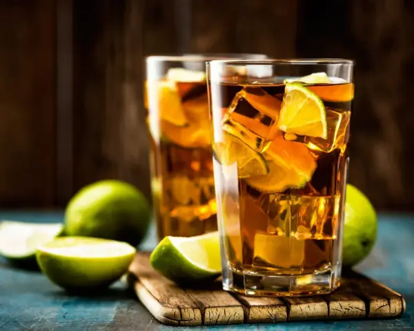 Dwa orzeźwiające drinki: Long Island Iced Tea czy Tokyo Tea, z lodem i limonką, na drewnianej desce.