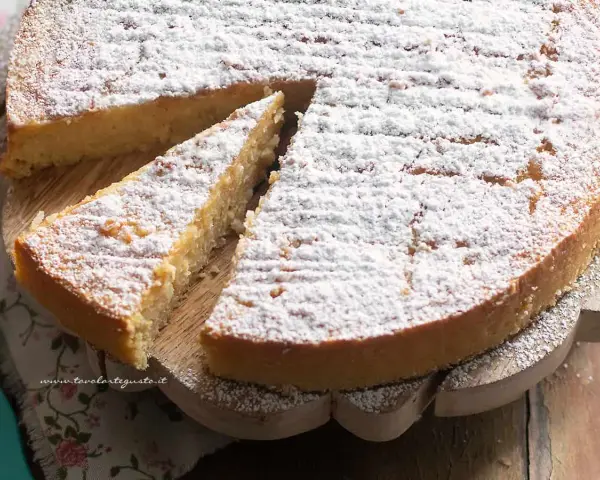 Una deliziosa torta di riso, cosparsa di zucchero a velo, su un tagliere di legno. Una fetta è già stata servita.