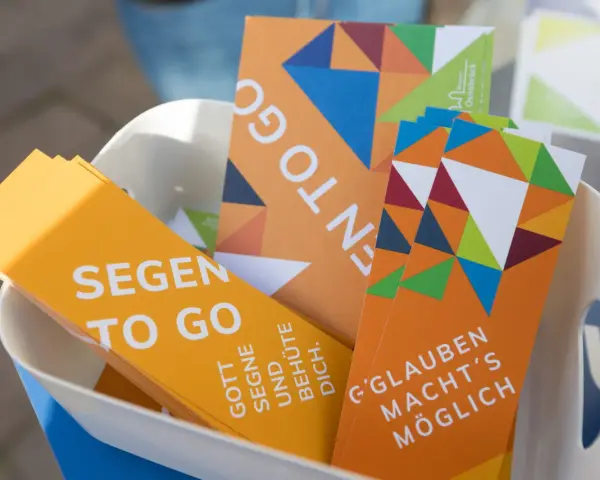 Bunte Karten mit der Aufschrift "Segen to go" und inspirierenden Botschaften wie "Gott segne und behüte dich" liegen in einem Korb.