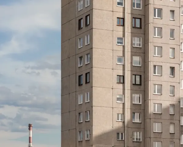 Szare bloki mieszkalne, każde mieszkanie od miasta z oknami wychodzącymi na niebo. W oddali widać komin.