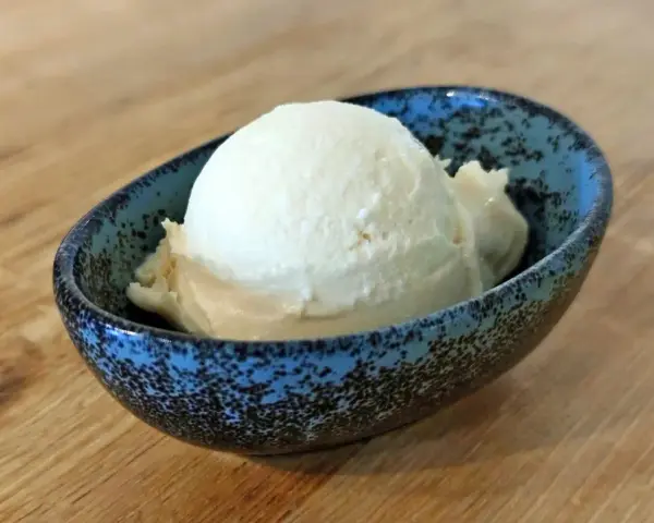 Ein Löffel cremiges Mandel Eis in einer blauen Schale auf Holztisch.