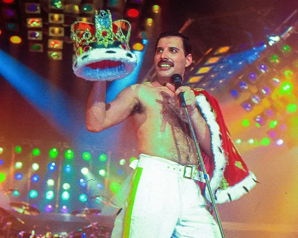 Freddie Mercury, król sceny, w koronie i z mikrofonem, na tle kolorowych świateł.