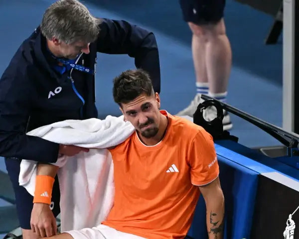 Tenisista z pomarańczową opaską na przedramieniu podczas Australian Open 2024 otrzymuje pomoc od fizjoterapeuty.