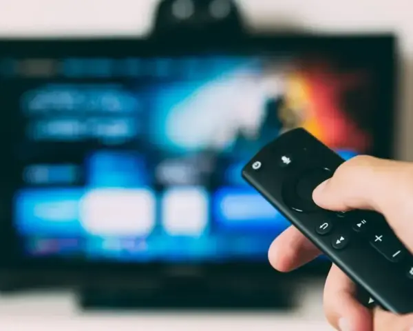 Dłoń trzymająca pilot do telewizora LG, ekran pokazuje menu. Dowiedz się, jak wyłączyć lektora w telewizorze LG.