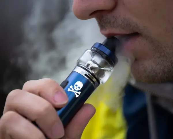 Persona vapeando un dispositivo con calavera, advirtiendo sobre los vapear efectos secundarios.