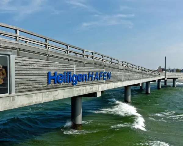 Hol dir die besten heiligenhafen tipps! Die Seebrücke mit dem Schriftzug "Heiligenhafen" ragt ins grüne Meer.