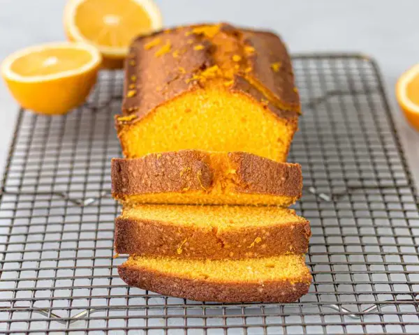 Un delicioso bizcocho de naranja, recién horneado y cortado en rebanadas, reposa sobre una rejilla.