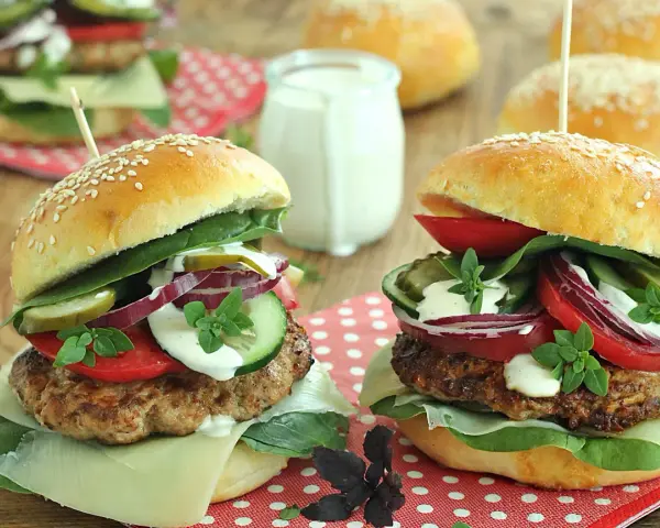 Dwa soczyste burgery wołowe z dodatkami na drewnianym tle.