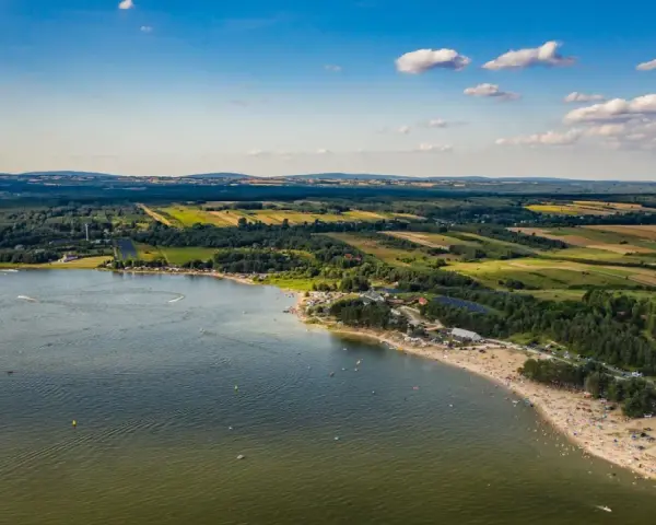 Letnie słońce nad **Jeziorem Chańcza**. Tłumy plażowiczów, zielone lasy i pola tworzą malowniczy krajobraz.