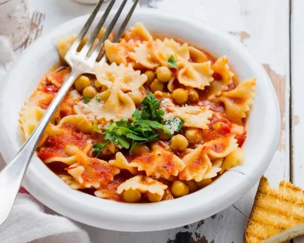 Farfalle-Pasta mit Kichererbsen in Tomatensauce, garniert mit Petersilie und Parmesan. Ein einfaches ceci rezept, perfekt für ein schnelles Mittagessen.