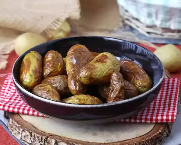 Patate novelle dorate e croccanti, appena sfornate dalla friggitrice ad aria, servite in una ciotola scura su un tagliere di legno.
