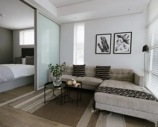 Nowoczesny salon z przesuwnymi drzwiami, za którymi widać sypialnię. Sofa, stoliki, obrazy.