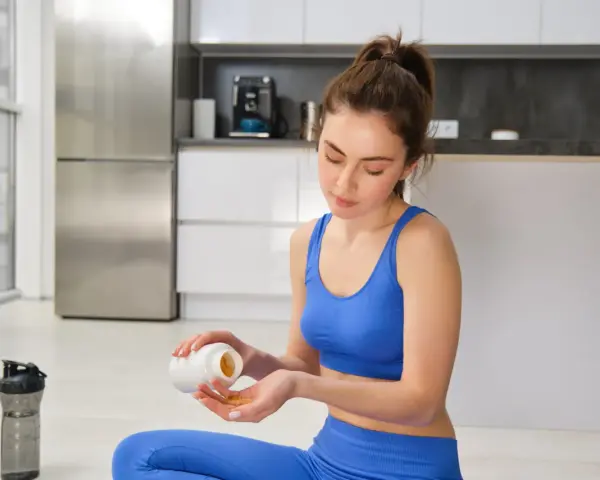 Femme en tenue de sport bleue prend des gélules, espérant un vitamine b12 effet immédiat pour son bien-être.