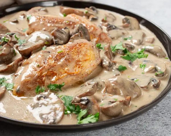 Un plat de poulet à la crème onctueuse, parsemé de champignons et de persil frais. Un délice crémeux qui invite à la dégustation.
