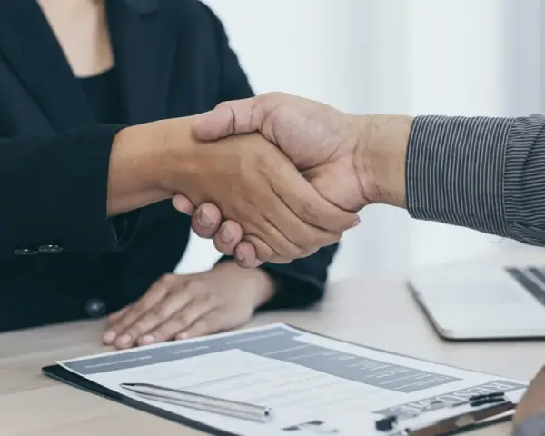 Dos personas se dan la mano sobre un escritorio con un currículum y un portátil. Es el final de una entrevista en francés.